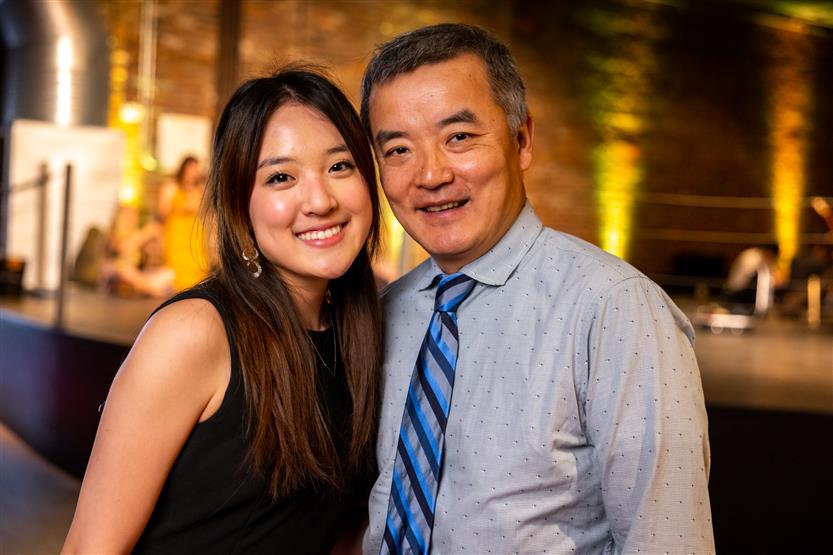 A young woman wearing black smiles with a man wearing a grey-blue shirt